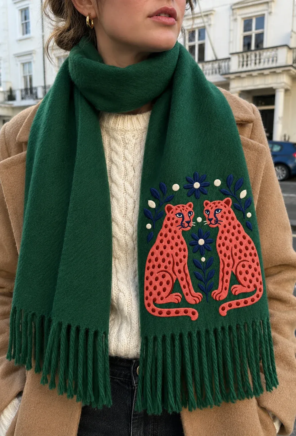 A woman on a city street in a forest-green scarf with two leopards above the fringe