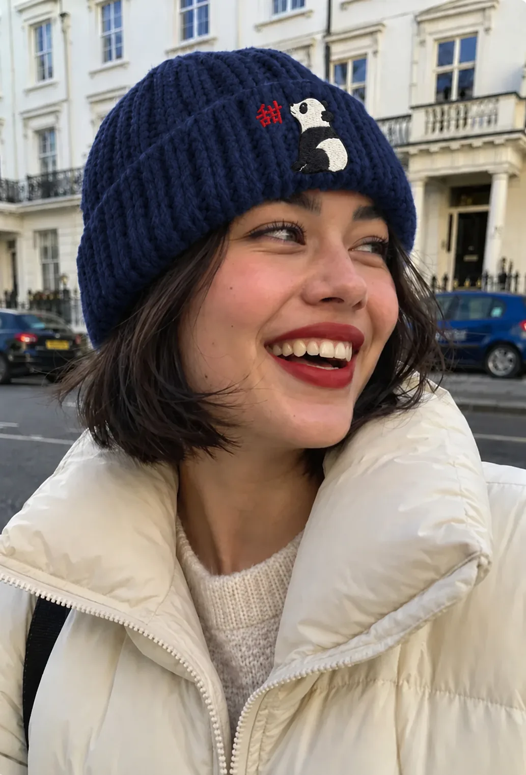 A laughing woman in a navy beanie with an ink panda on the cuff